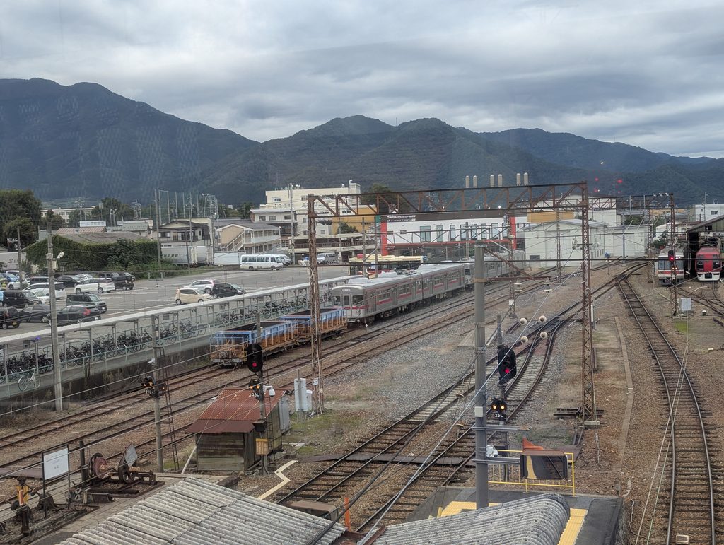 須坂駅構内に広がる線路と信号機、銀色の列車と山並み