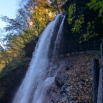 青空と色づき始めた木々を背景に流れ落ちる高山村の雷滝
