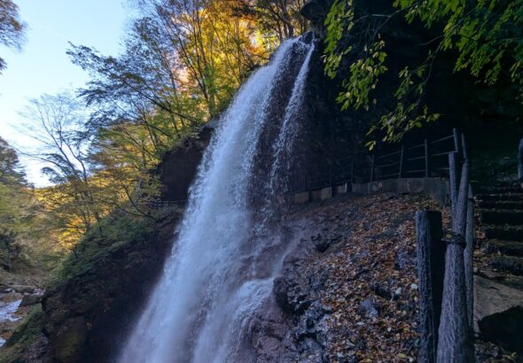 青空と色づき始めた木々を背景に流れ落ちる高山村の雷滝