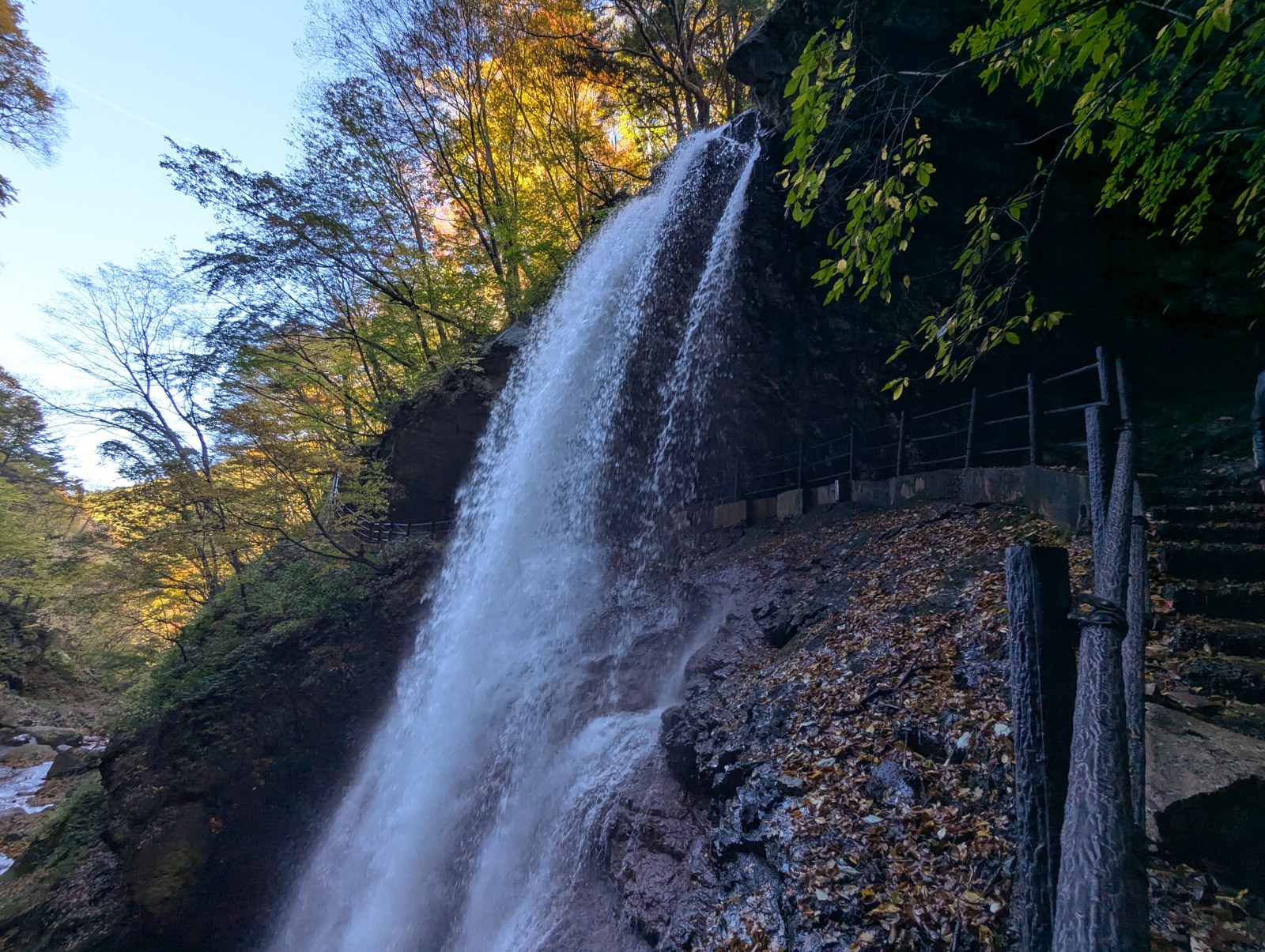 青空と色づき始めた木々を背景に流れ落ちる高山村の雷滝